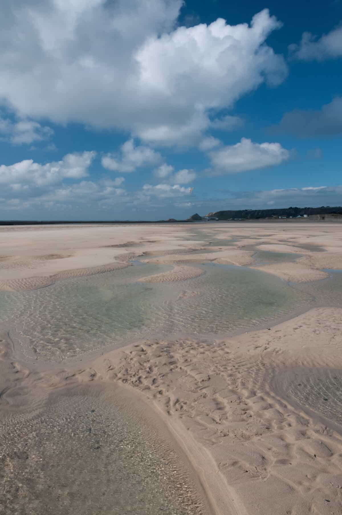 Fluffy clouds and sand patterns on the beach at St. Ouen's Bay