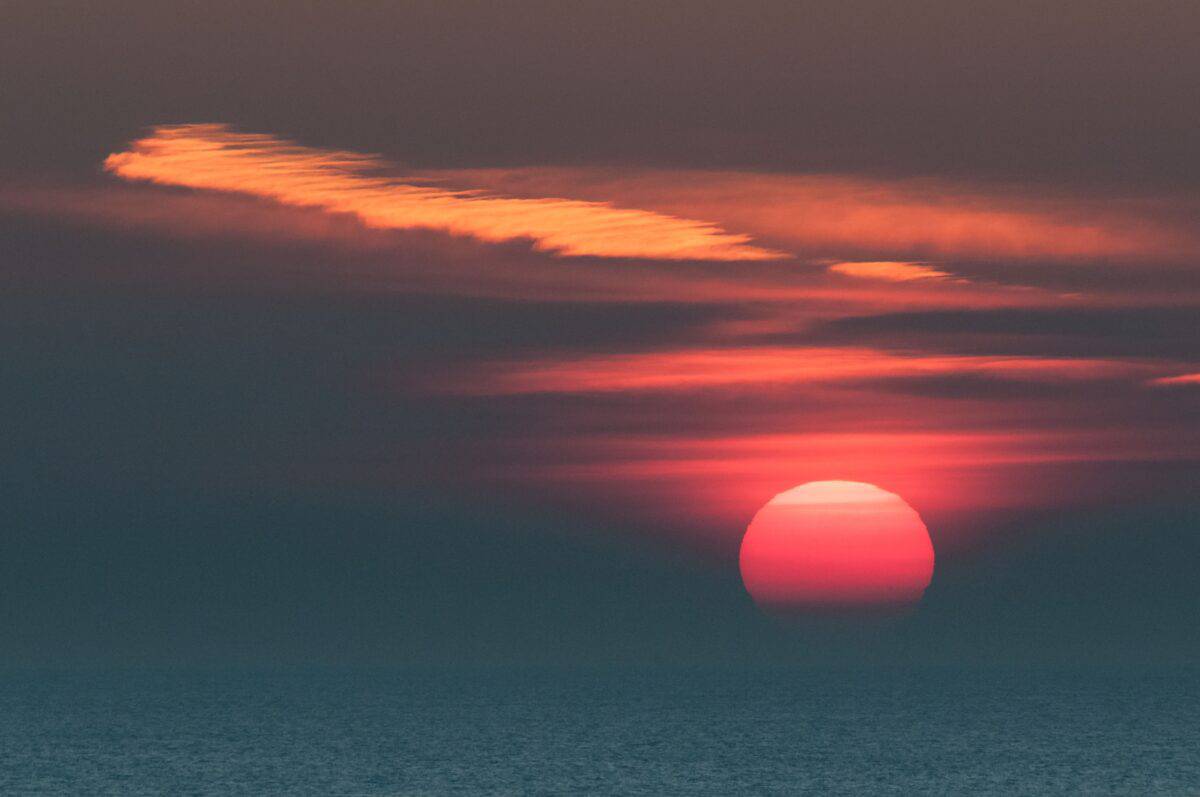 Strange clouds and a giant pink sun as the sun sets over the sea