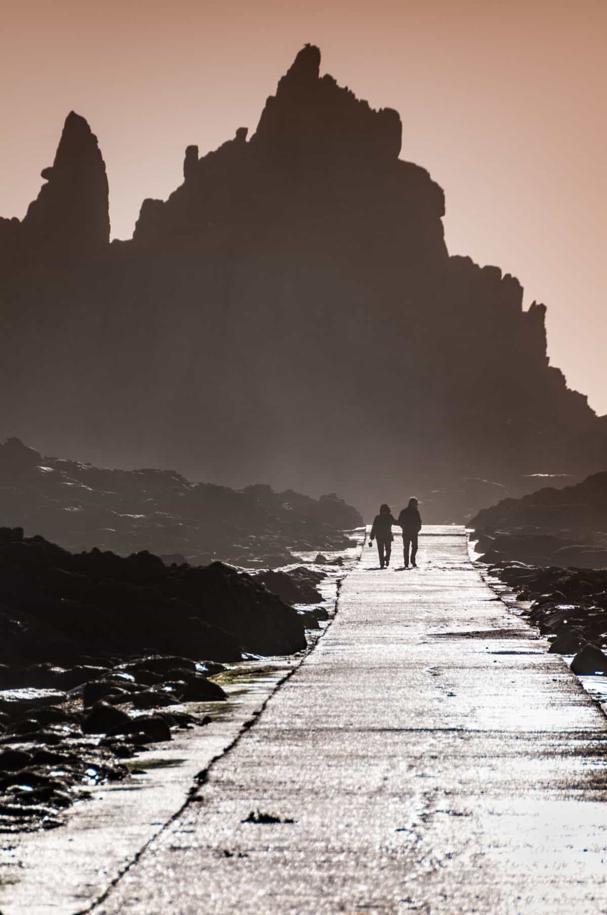 Couple silhouetted by rocks at Corbière Lighthouse causeway